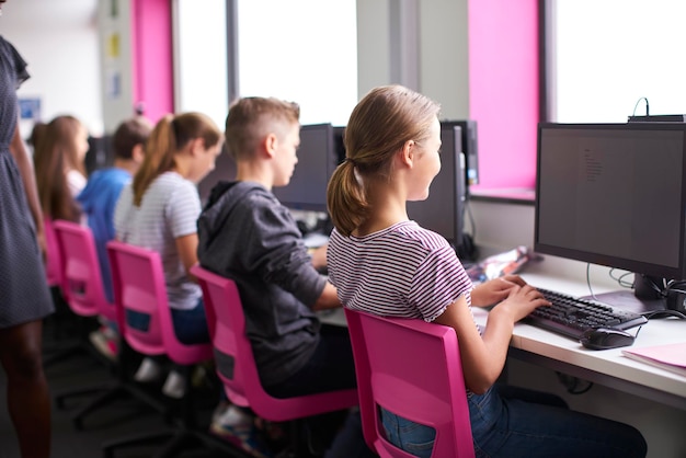 Achteraanzicht van vrouwelijke leraar die toezicht houdt op de lijn van middelbare scholieren die werken op schermen in de computerklas