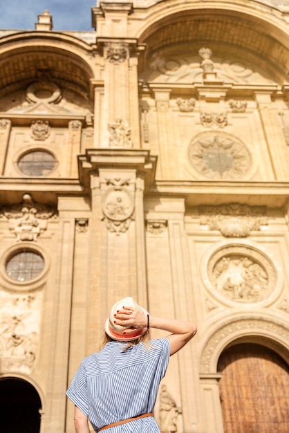 Achteraanzicht van vrouwelijke toeristenvrouw die haar hoed vasthoudt voor de kathedraal in Granada, Spanje