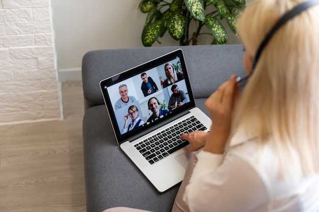 Achteraanzicht van zakenvrouw die met haar collega's praat over plan in videoconferentie. Multi-etnisch business team met behulp van laptop voor een online vergadering in video-oproep. Groep mensen slim thuiswerken