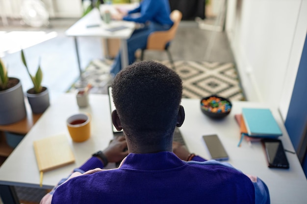 Achteraanzicht van zwarte man aan het werk aan een bureau in een leuke niet-conventionele kantoorruimte