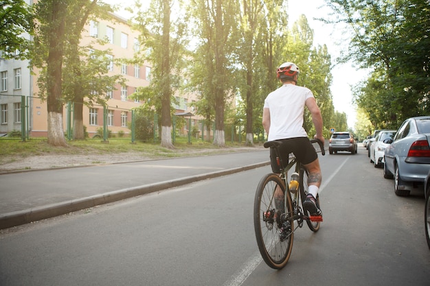 Achteraanzicht volledige lengte shot van een mannelijke fietser in fietshelm fiets in de stad