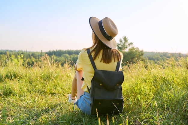 Achteraanzicht vrouw met rugzak in hoed genieten van zomerlandschap van wilde natuur