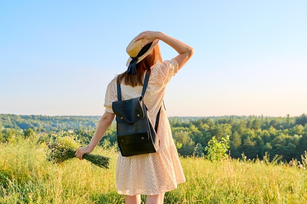 Achteraanzicht vrouw met rugzak in hoed genieten van zomerlandschap van wilde natuur