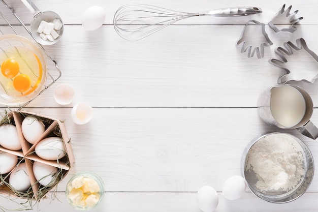 Achtergrond bakken. Koken ingrediënten voor deeg en gebak, eieren, bloem en koekjesvormer op wit rustiek hout. bovenaanzicht