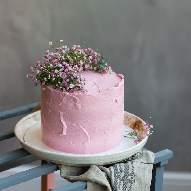 Achtergrond met roze slagroomtaart versierd met kleine bloemen, grijs tafelkleed en tafel in Scandinavische stijl