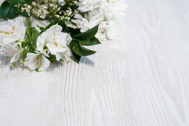 Achtergrond met witte bloemen en groen blad in hoeken op houten witte tafel