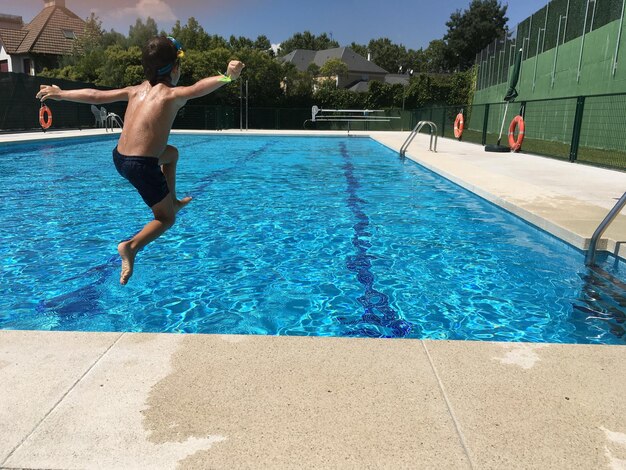 Foto achtergrond van een hemdloze jongen die in het zwembad van een resort springt