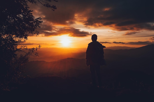 Achtergrond van een man die tijdens de zonsondergang op de berg tegen de hemel staat