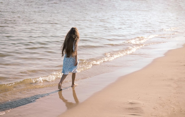 Achtergrond van een schattig klein meisje met lang haar in een witte jurk die op een tropische strandvakantie loopt