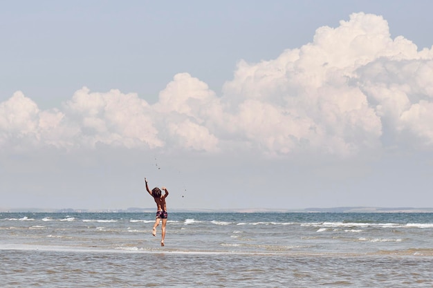 Achtergrond van een shirtloze jongen die in de zee springt tegen een bewolkte lucht
