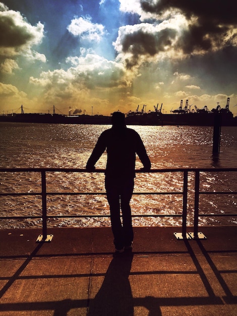 Foto achtergrond van een silhouetman die tijdens de zonsondergang op de pier tegen de rivier staat