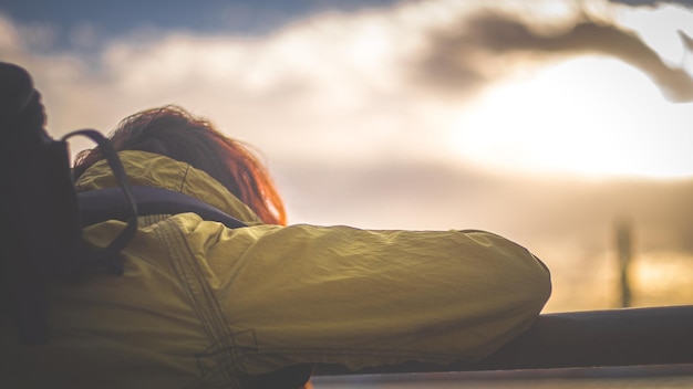 Achtergrond van een vrouw in een geel jasje die de hemel bij zonsondergang bekijkt