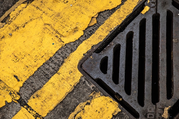 Achtergrond van het onweersafvoerkanaal en gele wegmarkeringen op het oude asfalt