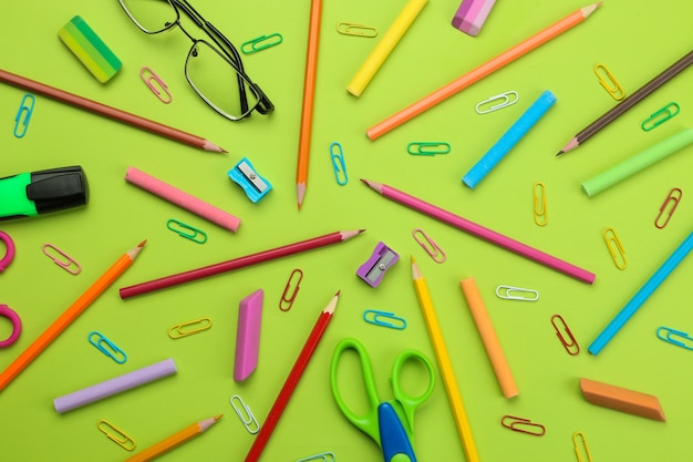 Achtergrond van verschillende schoolbenodigdheden potloden, paperclips, kleurpotloden op een felgroene achtergrond. Office-hulpmiddelen. onderwijs. bovenaanzicht.