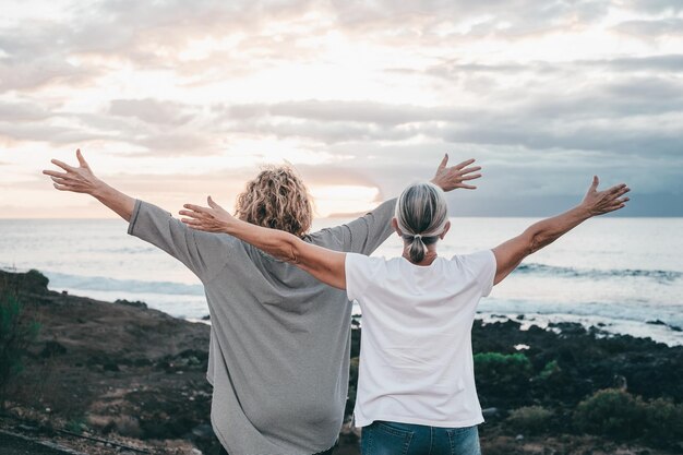 Foto achtergrond van volwassen en oudere vrouwen die met uitgestrekte armen tegen de zee staan en naar de horizon kijken