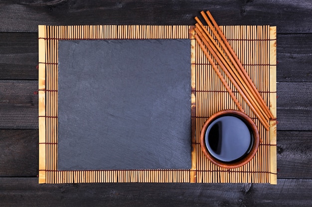 Achtergrond voor sushi. Bamboe mat en sojasaus op zwarte houten tafel. Bovenaanzicht en kopie ruimte