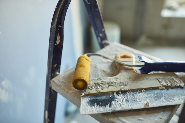 Achtergrondafbeelding van gebruikte spatel en verfroller liggend op de ladder op de bouwplaats of in woningbouw, kopie ruimte