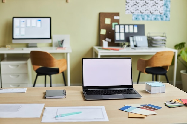 Achtergrondafbeelding van gezellig kantoorinterieur met ontwerperswerkplek en open laptop wit scherm mock