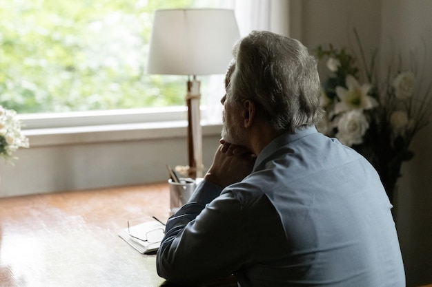 Achtergrondbeeld van een bejaarde grijze man die naar het raam kijkt en nadenkt