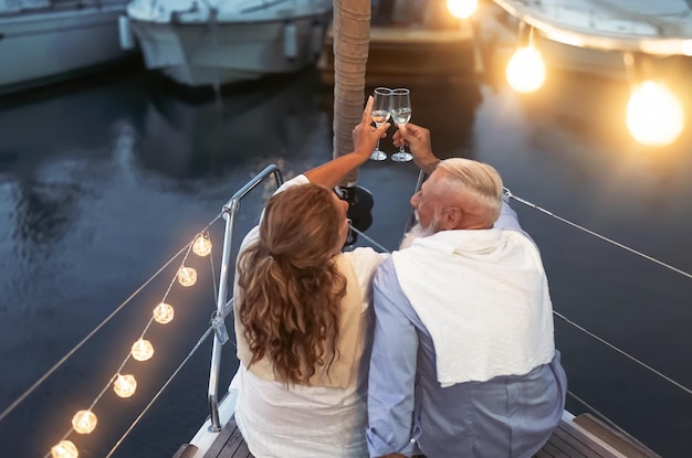 Foto achtergrondbeeld van een echtpaar met champagne in de hand terwijl ze op het verlichte bootdek zitten