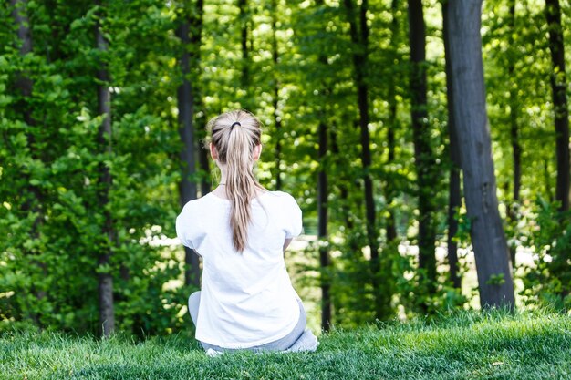 Achtergrondbeeld van een jonge vrouw die op een grasveld in het bos zit