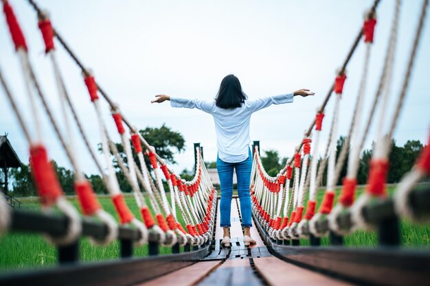 Foto achtergrondbeeld van een jonge vrouw met uitgestrekte armen die op een voetgangersbrug tegen de lucht staat