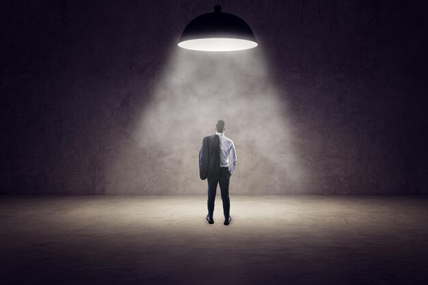 Achtergrondbeeld van een jonge zakenman die in het schijnlicht van een lamp in een betoninterieur staat