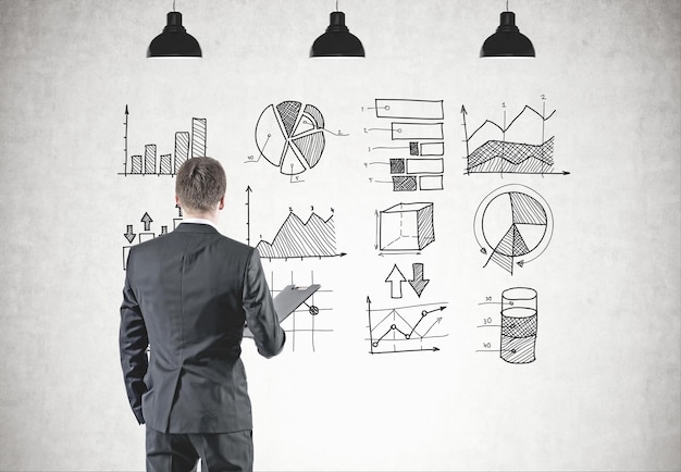 Achtergrondbeeld van een jonge zakenman in een grijs pak die een map vasthoudt. Hij kijkt vooruit. Grafieken en diagrammen getekend op een betonnen muur