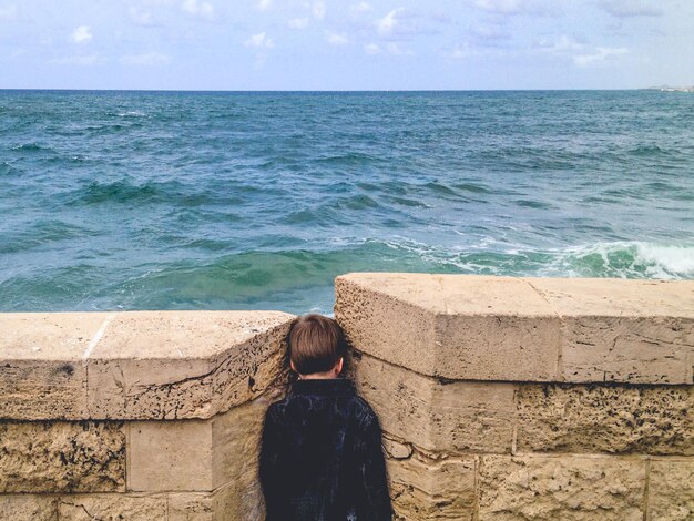 Achtergrondbeeld van een jongen die midden in een steunmuur tegen de zee staat