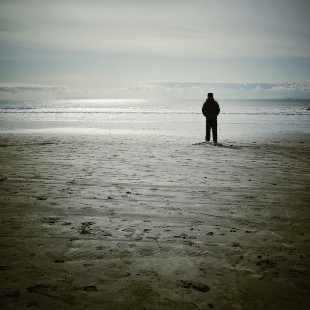 Achtergrondbeeld van een man die bij zonsondergang op het strand staat