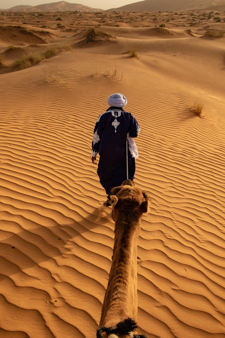 Foto achtergrondbeeld van een man die met een kameel op het zand loopt