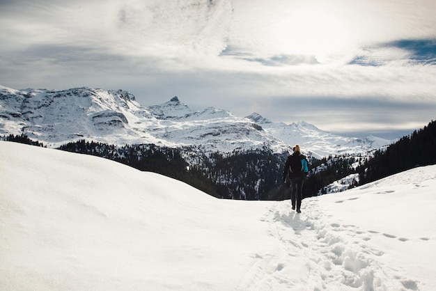 Achtergrondbeeld van een man die op een met sneeuw bedekt veld loopt door bergen tegen de lucht