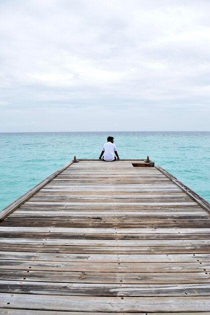 Achtergrondbeeld van een man die op een pier zit over de zee tegen de lucht