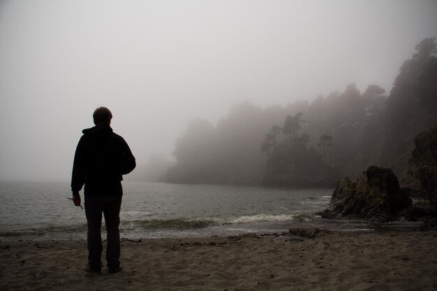 Foto achtergrondbeeld van een man die tijdens mistig weer naar de zee kijkt