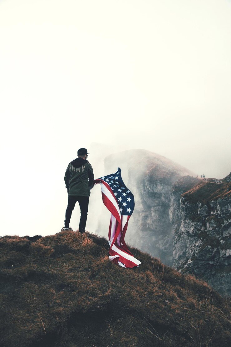 Foto achtergrondbeeld van een man met een amerikaanse vlag die op een berg tegen de lucht staat