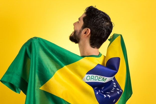 Foto achtergrondbeeld van een man met een braziliaanse vlag die tegen een gele achtergrond staat