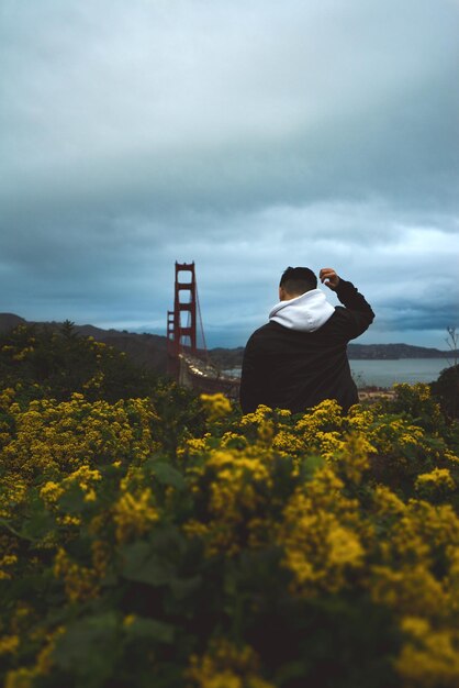 Foto achtergrondbeeld van een man met een kapje terwijl hij te midden van gele bloeiende planten op het veld tegen de golden gate bridge staat