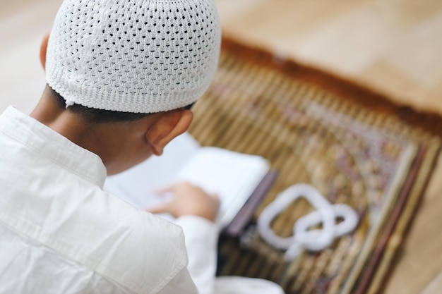 Foto achtergrondbeeld van een moslimkind met een schedelhoed die de koran op een gebedsmat in de moskee leest