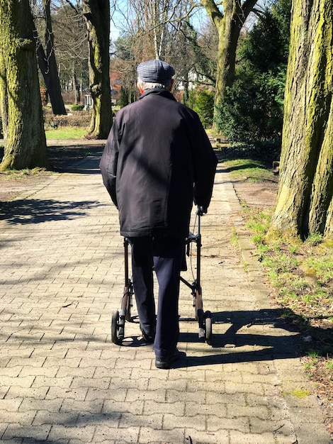 Foto achtergrondbeeld van een oudere man met een mobiliteitswandelaar op het voetpad in het park tijdens een zonnige dag