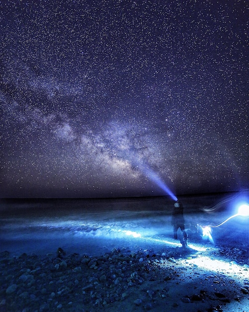 Foto achtergrondbeeld van een persoon die op de kust staat en een zaklamp vasthoudt tegen de melkweg