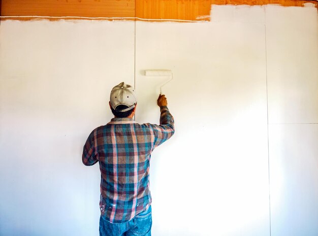 Foto achtergrondbeeld van een schilder die de houten muren van de kamer wit schildert met een verfroller