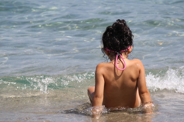 Foto achtergrondbeeld van een shirtloos meisje dat in de zee zit