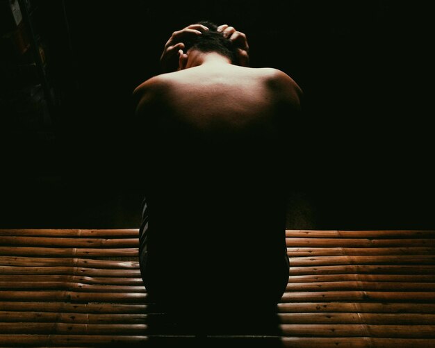 Foto achtergrondbeeld van een shirtloze depressieve man die in een donkere kamer zit