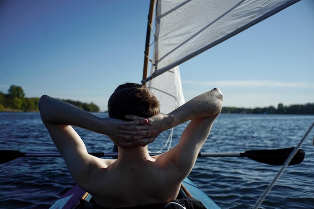 Foto achtergrondbeeld van een shirtloze jonge man die op een zeilboot in de zee tegen de lucht zit