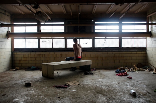 Foto achtergrondbeeld van een shirtloze man die in een verlaten kamer zit