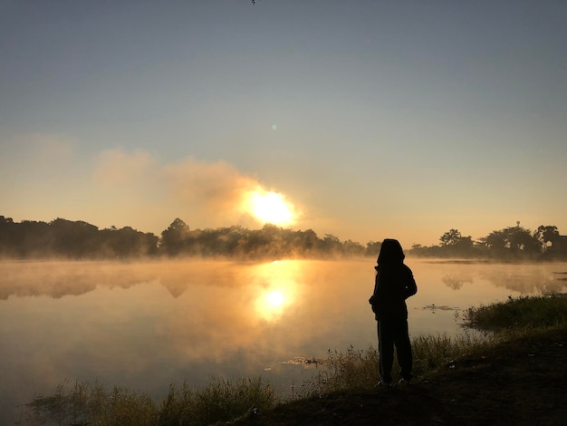 Achtergrondbeeld van een silhouet man die bij het meer staat tegen de hemel tijdens de zonsondergang