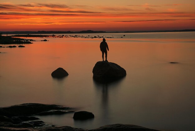 Achtergrondbeeld van een silhouet man die bij zonsondergang op een rots staat