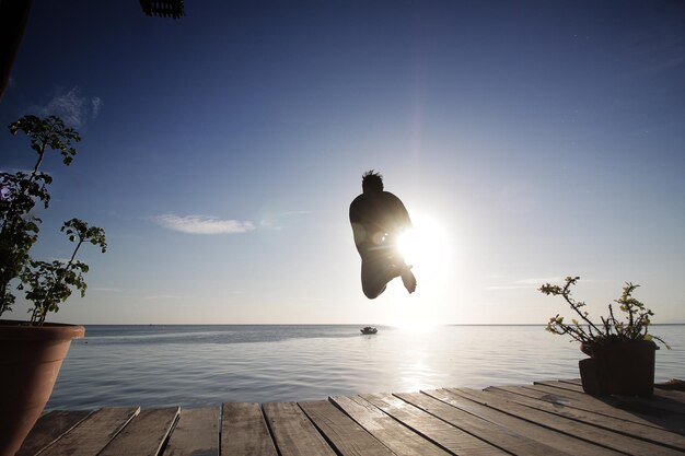 Achtergrondbeeld van een silhouet man die op een zonnige dag in de zee springt tegen de blauwe hemel