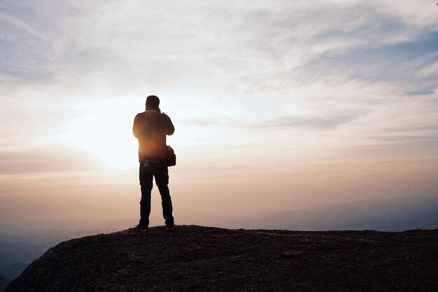 Foto achtergrondbeeld van een silhouet man die tijdens de zonsondergang op de berg staat