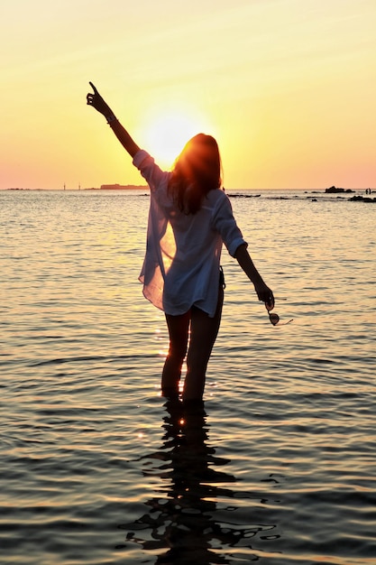 Achtergrondbeeld van een silhouetvrouw die in de zee staat tegen een oranje hemel